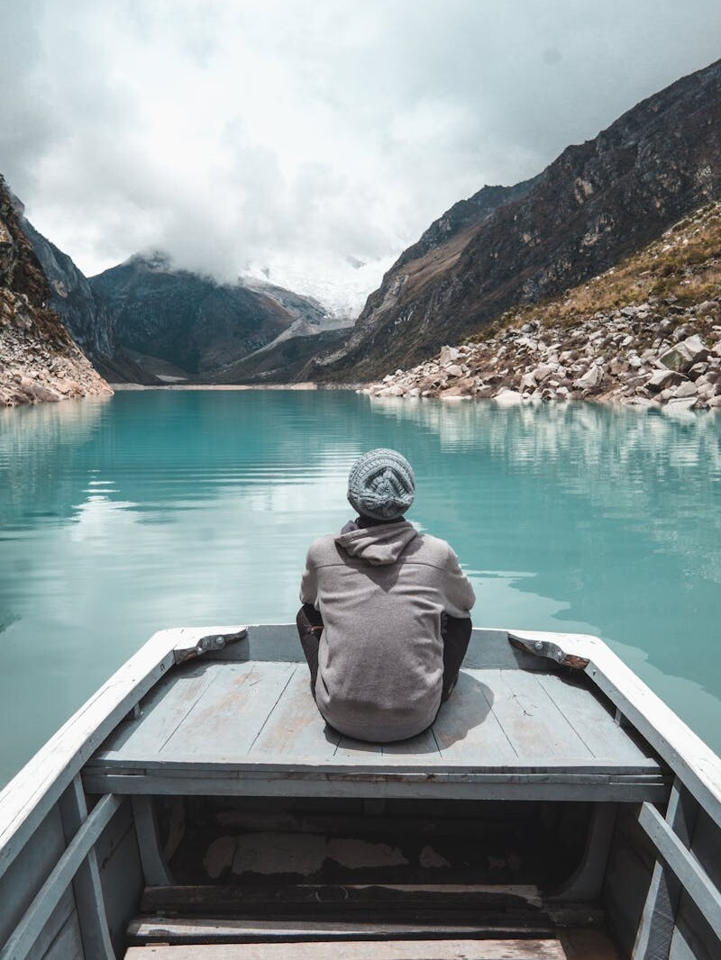 Contemplative view of a person on a boat in a serene lake surrounded by mountains in Huaraz, Peru.
