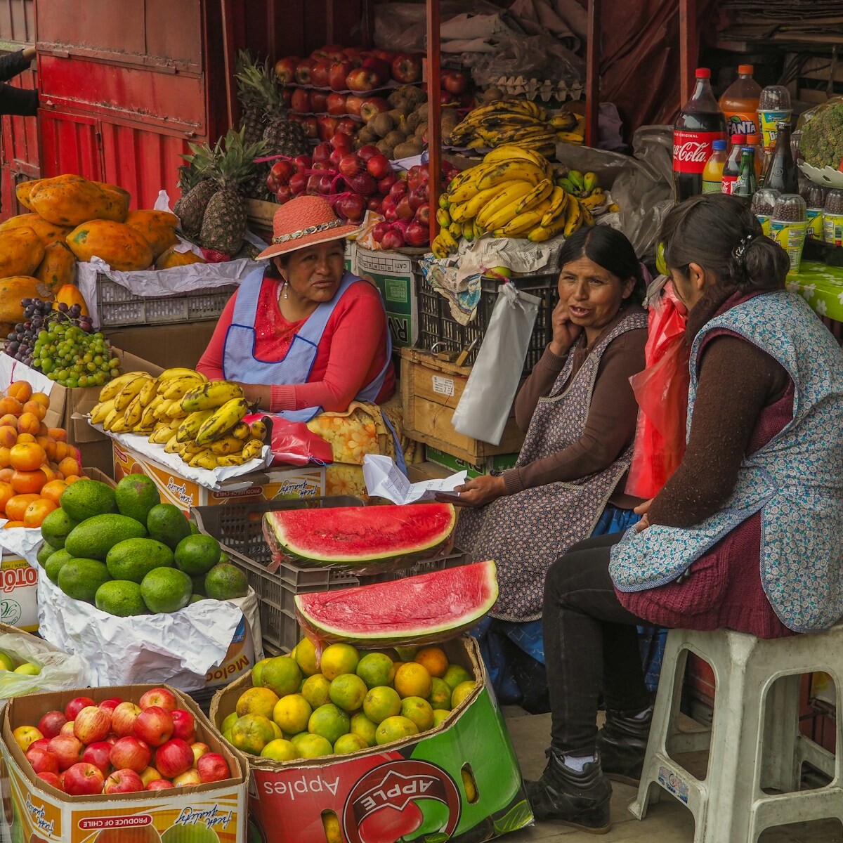 three women sitting behind assorted fruits on display in sidewalk